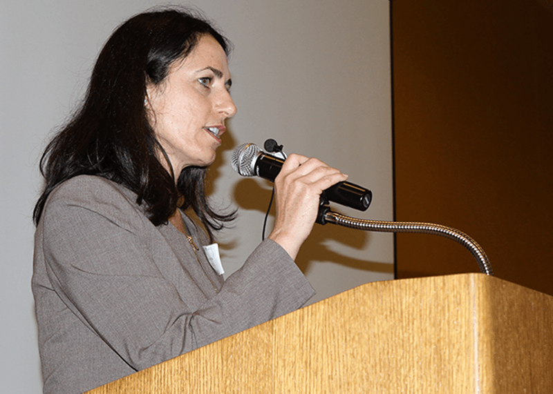 Natasha speaking in front of a microphone on a podium.